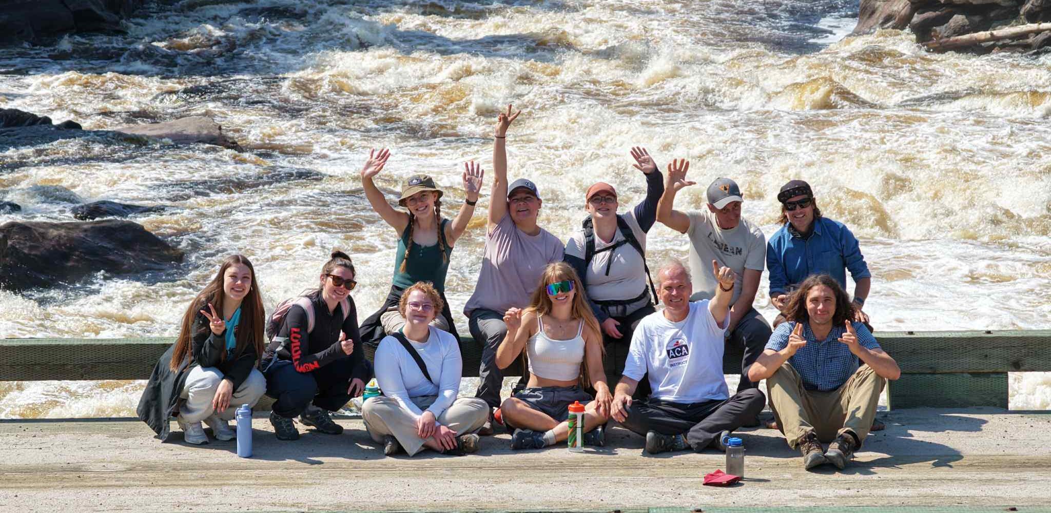 A group of youth and CPAWS staff pose for a photo standing on a bridge overlooking turbulent rapids below. 